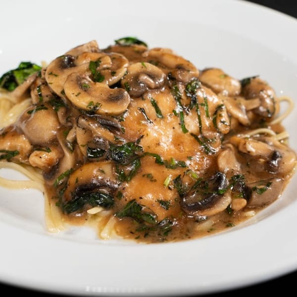 Giuseppe's chicken marsala with mushrooms and parsley over spaghetti on a white plate.