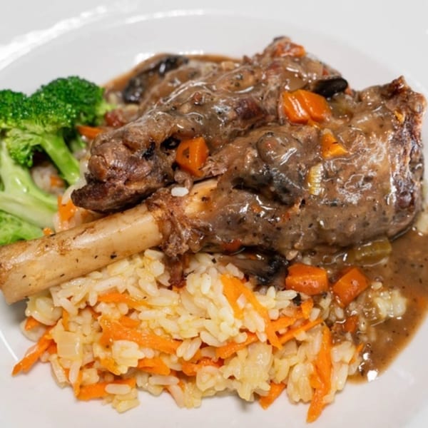Braised lamb shank with gravy, carrots, mushrooms, rice pilaf, and a side of broccoli.