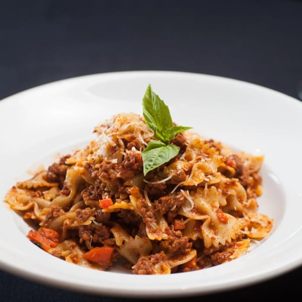 Giuseppe's farfalle pasta with meat sauce, parmesan, and basil on a white plate.