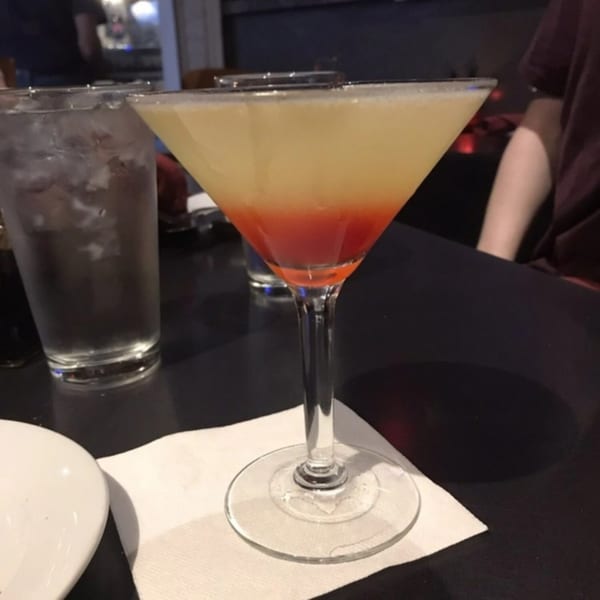 A vibrant, layered cocktail with yellow and red hues in a martini glass on a dark table.