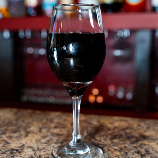 A glass of red wine sits on a speckled countertop with a blurred red background.