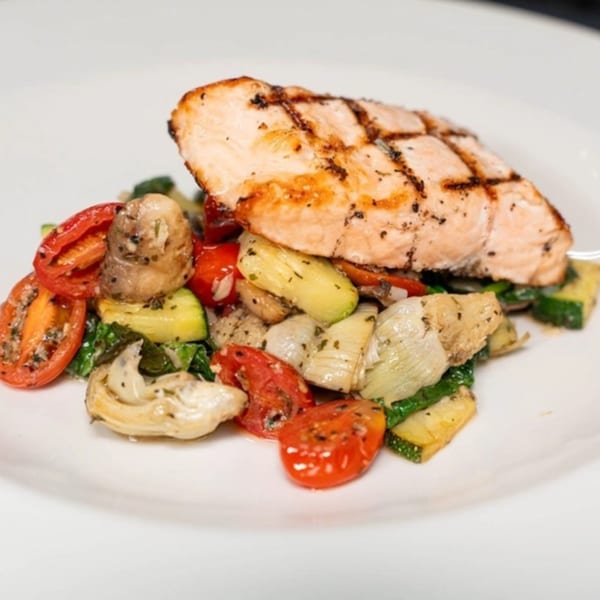 Grilled salmon fillet with roasted cherry tomatoes, zucchini, mushrooms, and artichoke hearts.