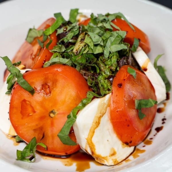 Caprese salad with sliced tomatoes, fresh mozzarella, basil, and balsamic glaze on a white plate.